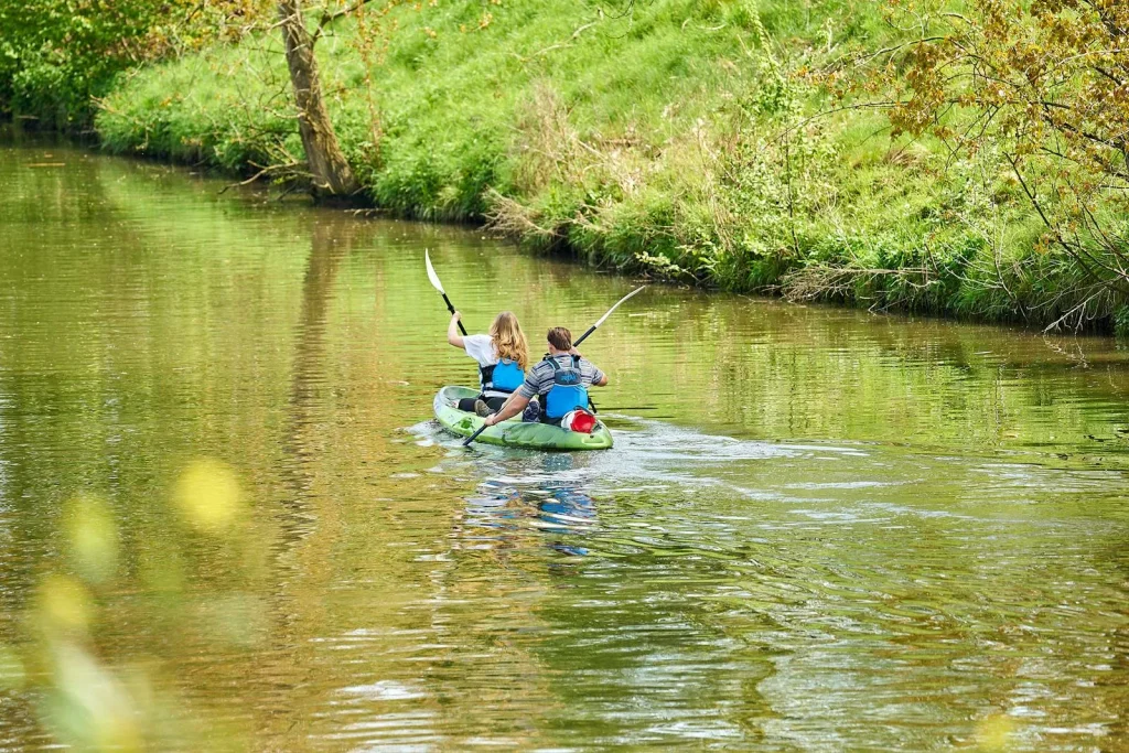 Couple paddling a tandem kayak together on a peaceful river surrounded by greenery
