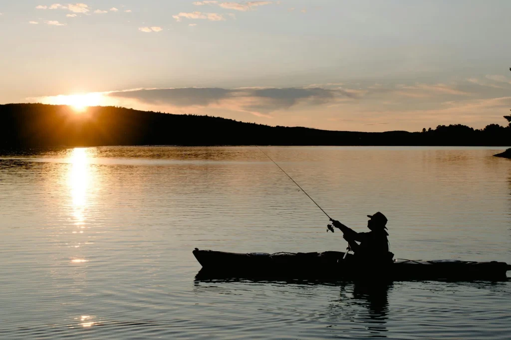 Angler fishing from a sit-on-top kayak on a calm UK lake at dawn