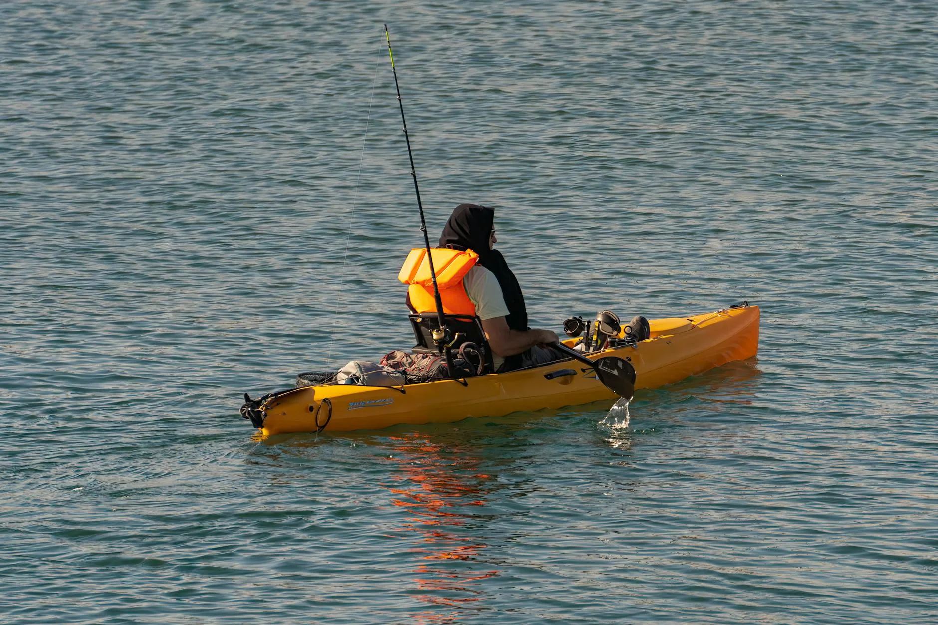 Angler paddling a fishing kayak along a tree-lined river