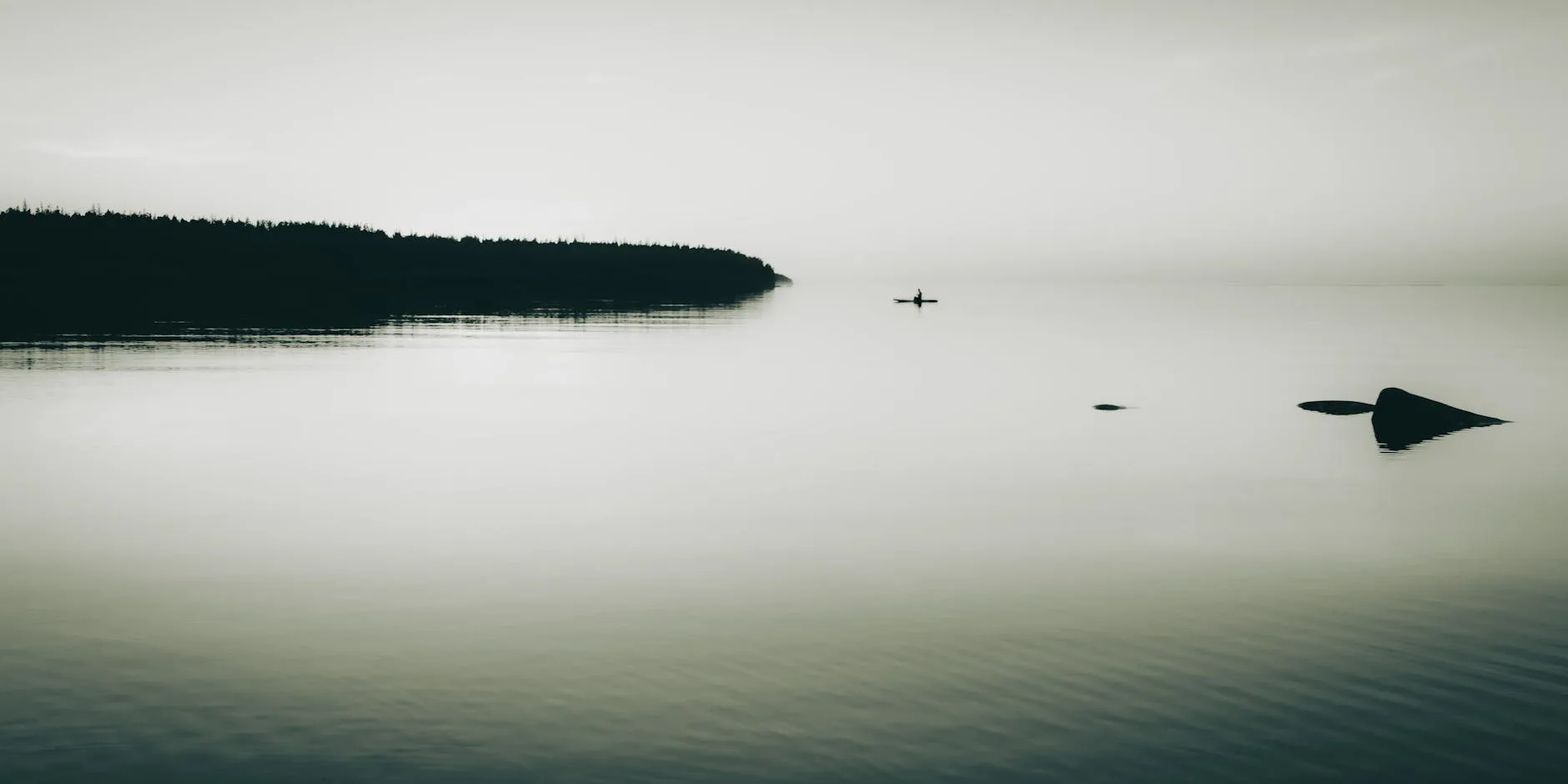 Person paddling a kayak on a calm lake with scenic surroundings