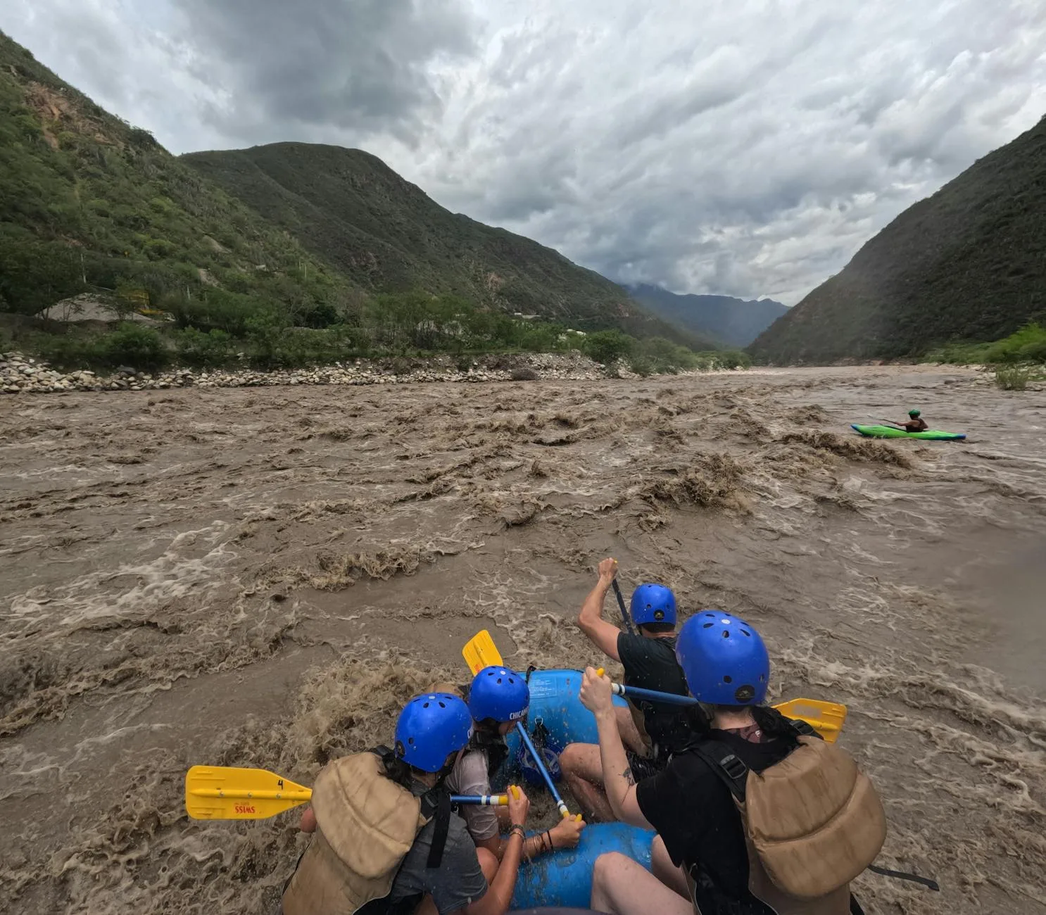Kayaker visible among whitewater rafters on rapids