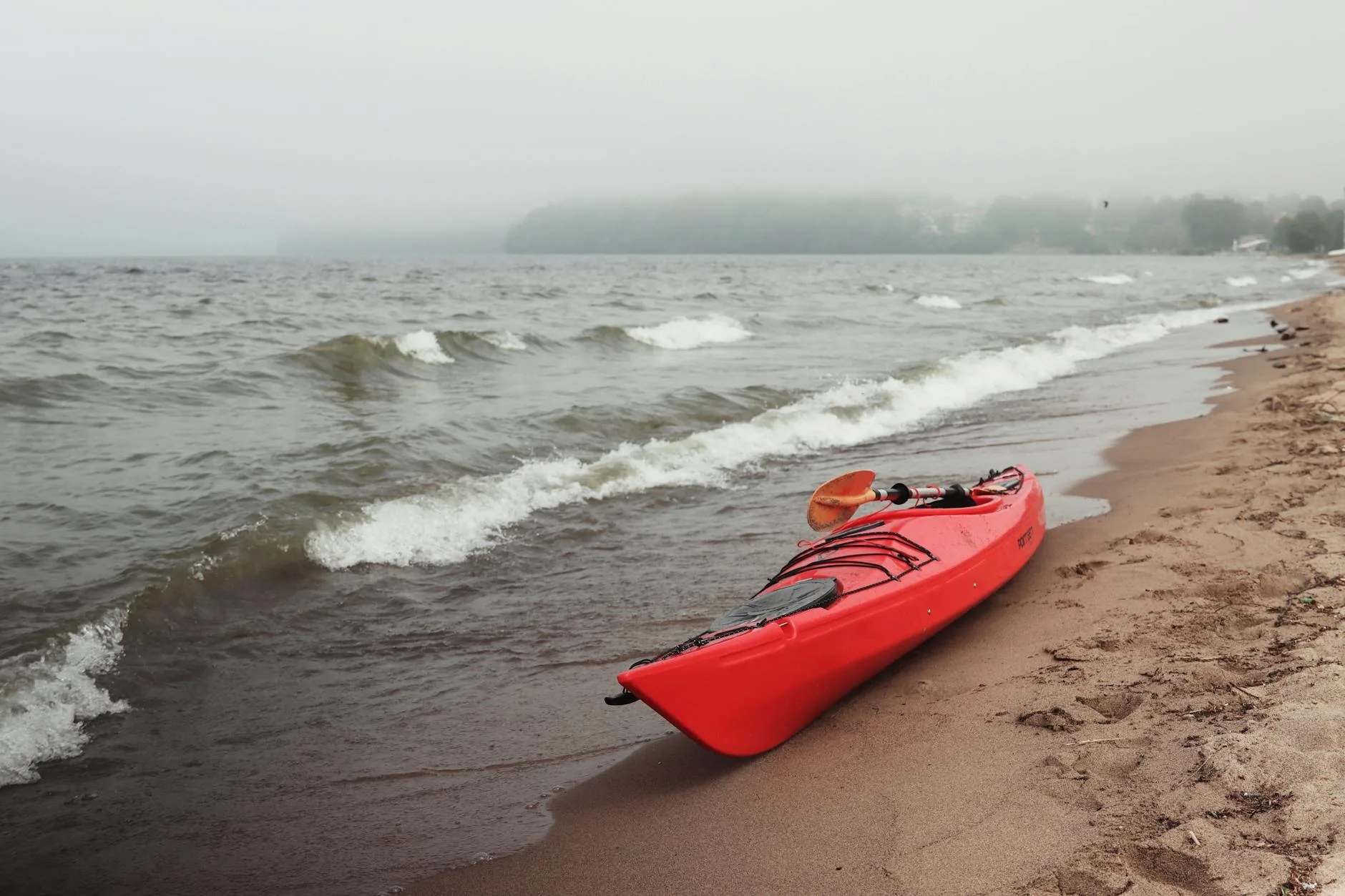 Red kayak resting on a sandy lake shore ready for paddling