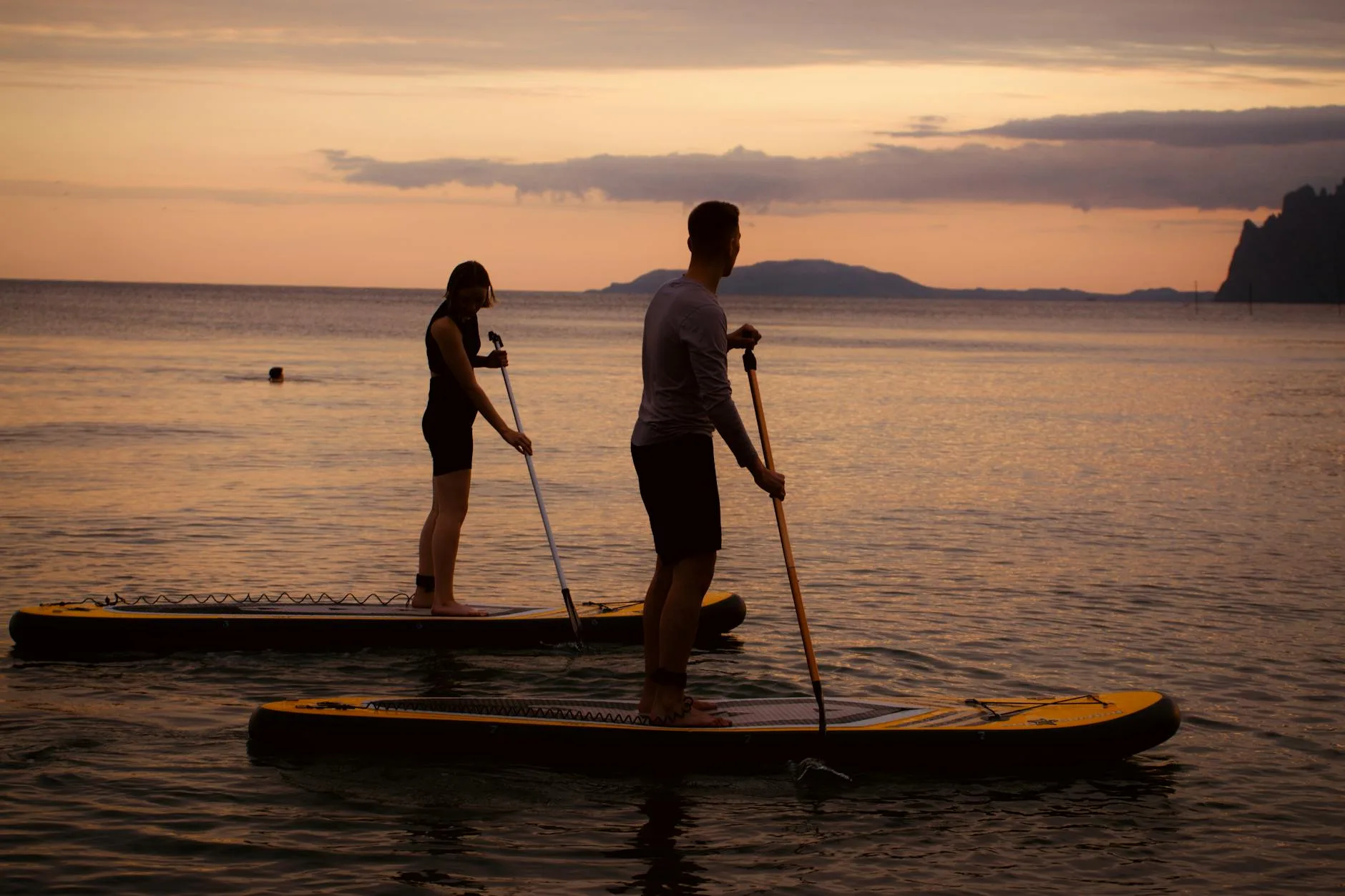Paddleboarder silhouetted against sunset on calm water
