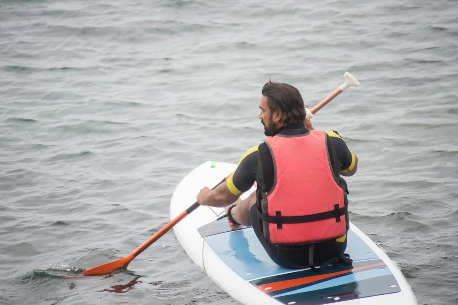 Paddleboarder in wetsuit performing a forward paddle stroke on open water