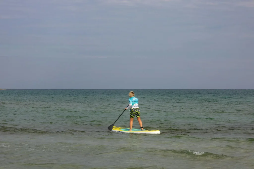 Beginner paddleboarder practising paddle stroke technique on calm sea