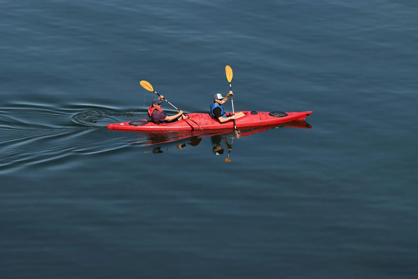 Two people paddling a red tandem kayak on a calm lake