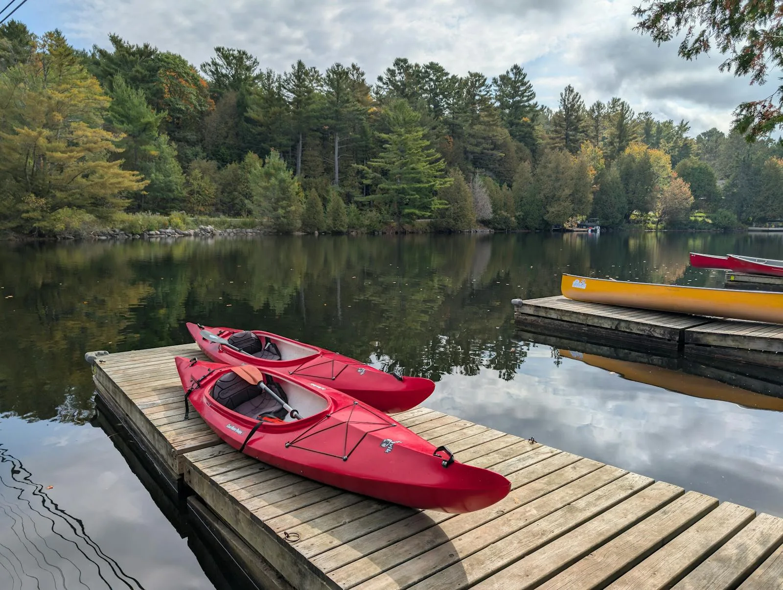 Two red kayaks resting on a wooden dock beside a calm forest-lined lake